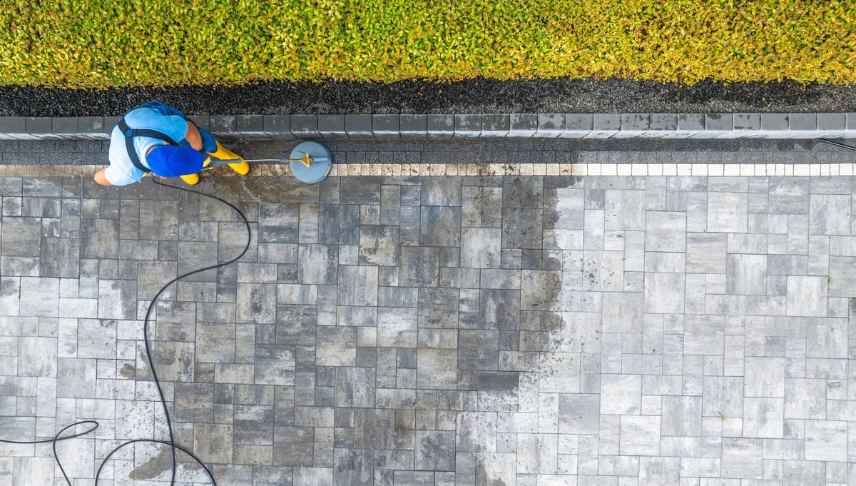A worker uses a pressure washer to clean a stone patio, revealing a fresh and tidy surface in a well-maintained outdoor area.